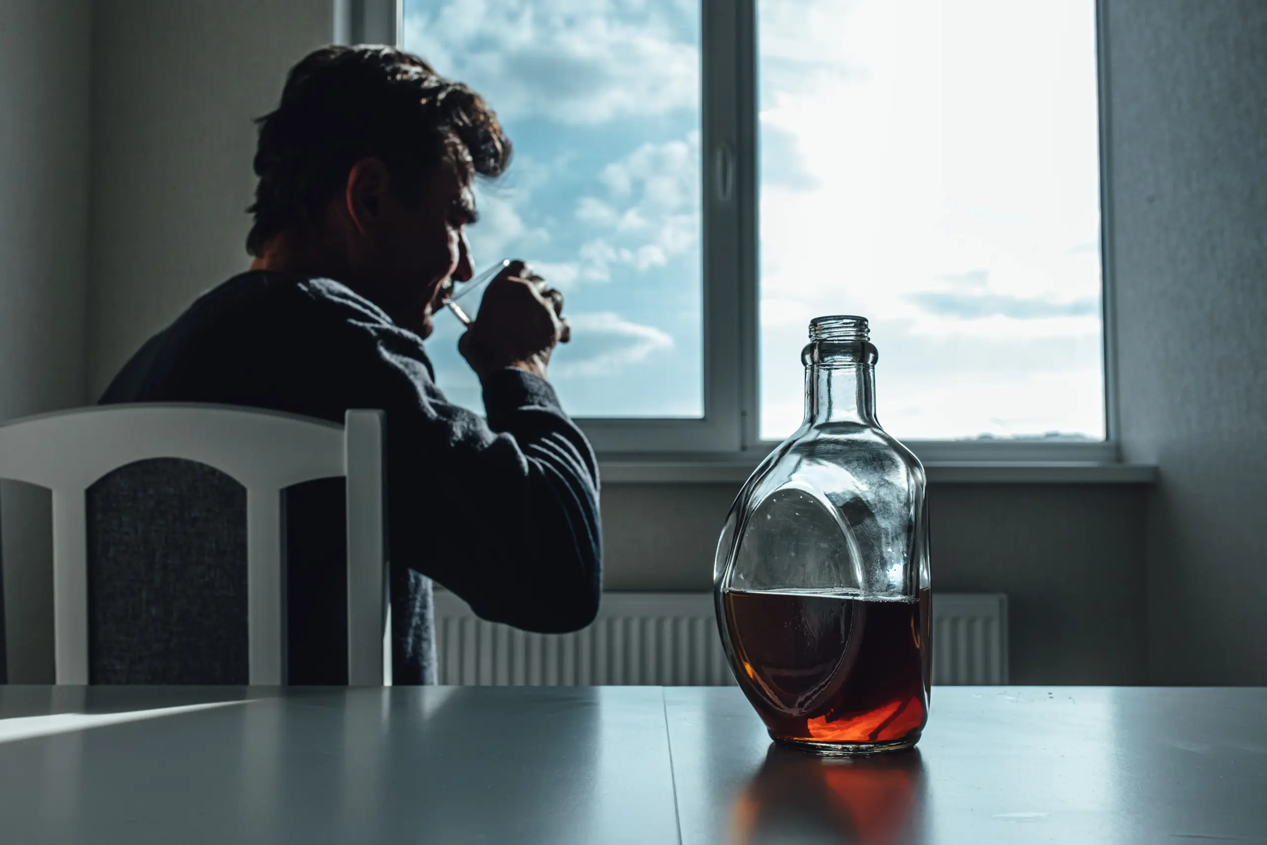 Depressed alcohol addict sitting near window