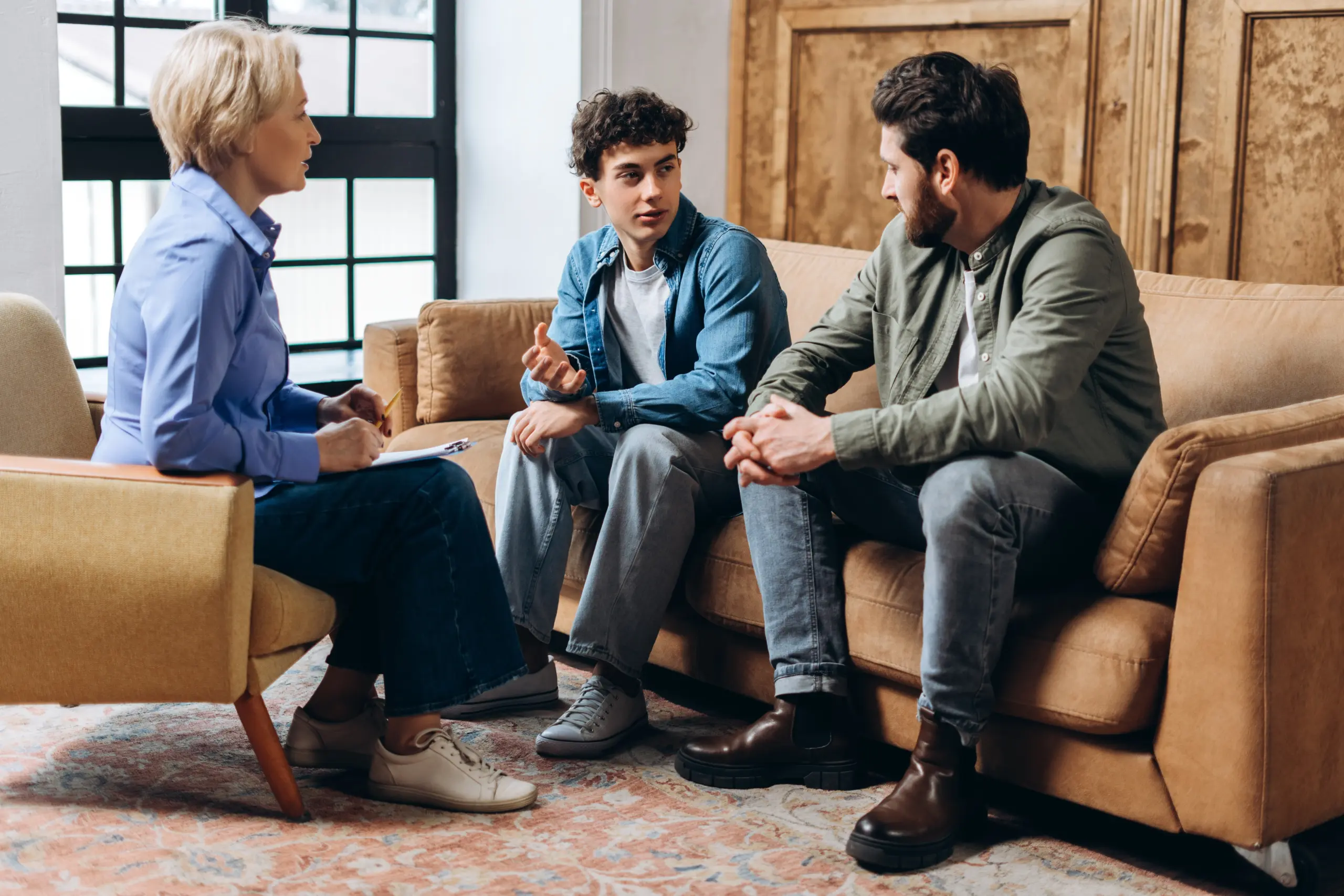 Father and teenage son visiting psychologist, talking together in the office. Family problems, teenage troubles, therapist, advice, help concept
